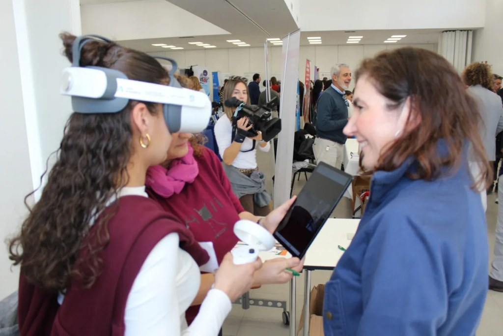Fotografiía en la que se puede ver a  una persona usando unas gafas de realidad virtual con la ayuda del personal de la Feria de Empleo.
